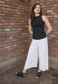 Taylor wears a small boatneck tank in black, paired with small white calypso linen pants.